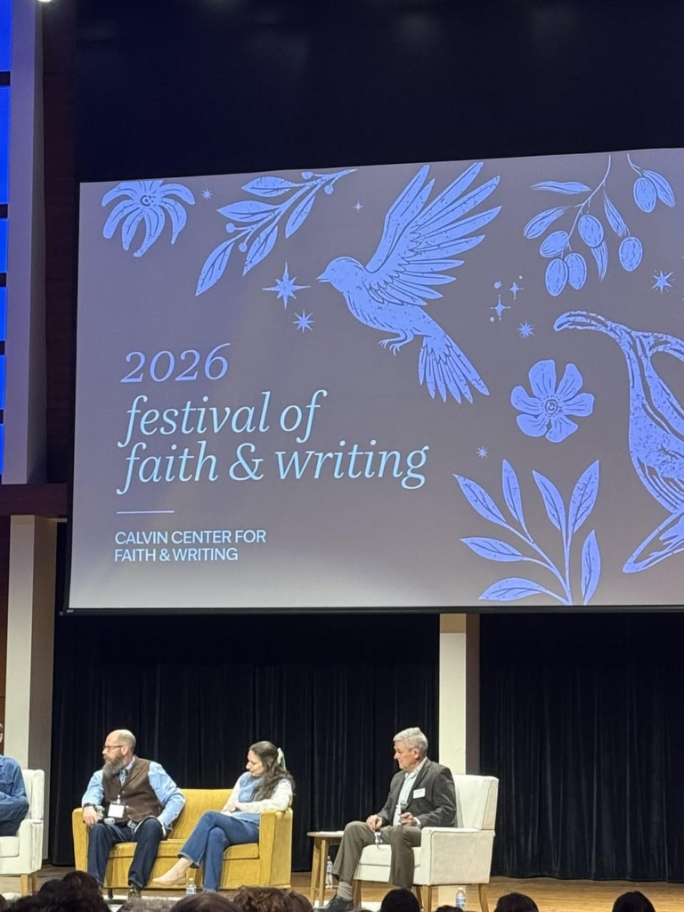 Image of a slide image with the words 2026 festival of faith and writing with three people on a stage under the image that is displayed on a large projection screen.