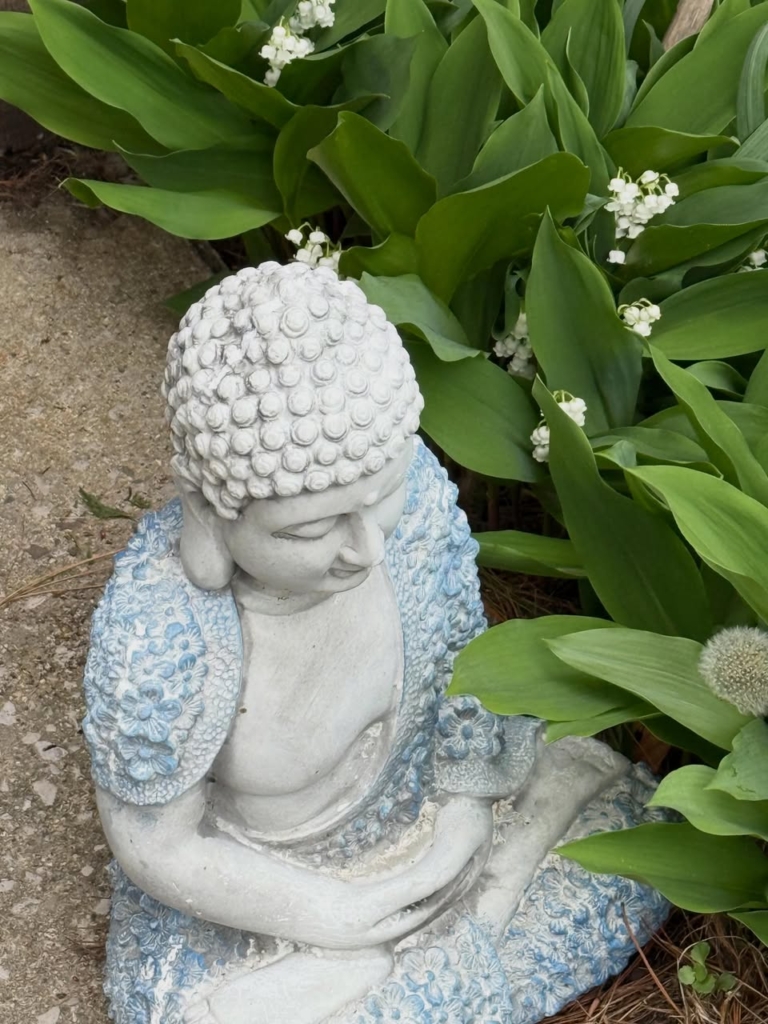 Image of a ceramic or concrete statue in the likeness of a mediating figure resting in what appears to be scorpion grass.